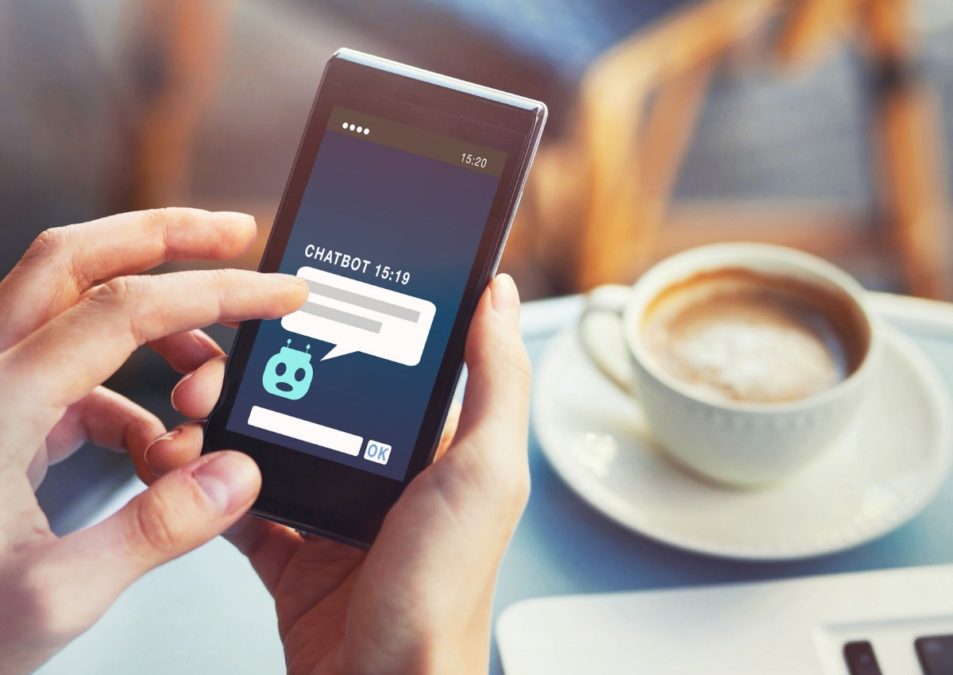 A photo of a person hands holding a mobile and touching it with the fingers, a cup of coffe on a table in the background