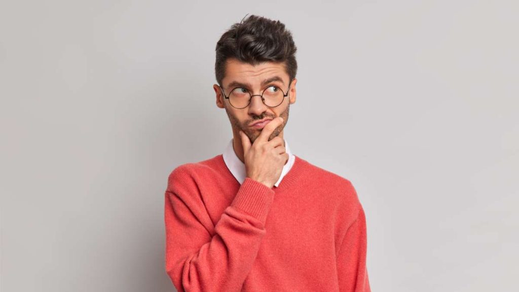 photo of a thoughtful adult european man holding his chin and looking pensively away as he tries to solve a problem